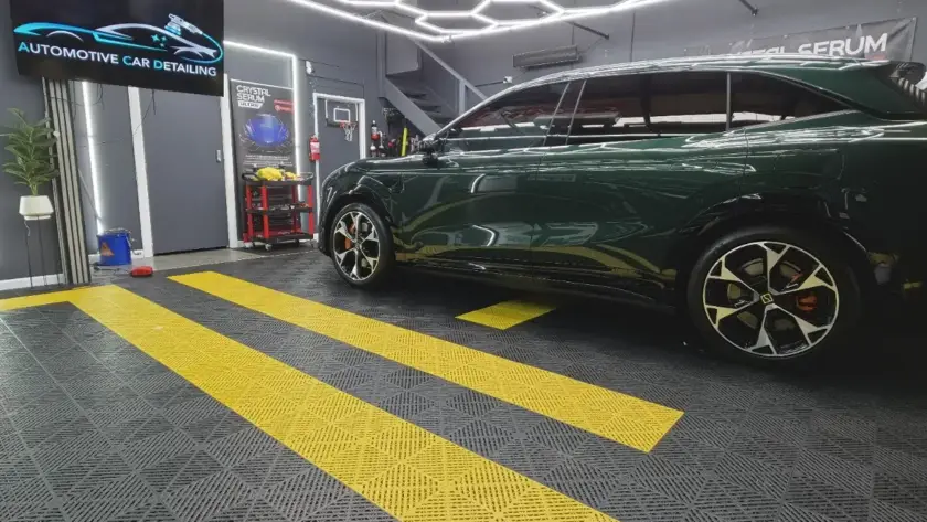 Modern car detailing garage with dark green SUV, logo screen, and unique floor tiles.