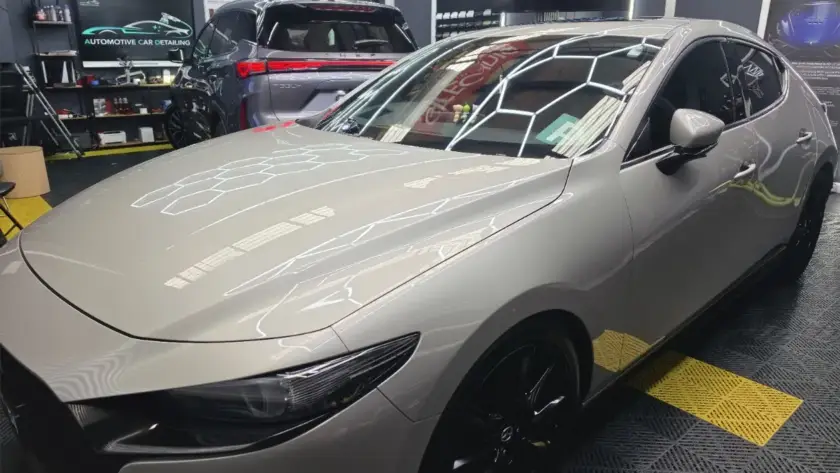Shiny light grey car with black wheels in a professional car detailing shop.