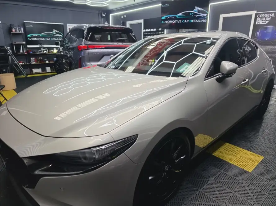 Shiny light grey car with black wheels in a professional car detailing shop.